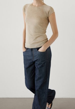 Beige top met korte mouwen gecombineerd met donkerblauwe jeans met wijde pijpen, met een gladde textuur en minimale stiksel details.
