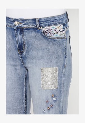 Lichtblauwe spijkerbroek van denim met een bloemen katoenen zak, een glanzend zilveren patch en geborduurde accenten in roze, oranje en wit.