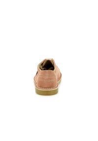 Chaussure en suede rose avec un bout arrondi, des détails de couture visibles et une semelle en caoutchouc beige. Le design présente une coupe basse et un style slip-on.
