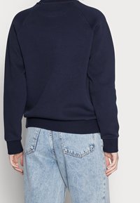 Sweat-shirt bleu marine à manches raglan, poignets et ourlet côtelés. Texture douce, coupe décontractée, associé à un jean bleu clair délavé.