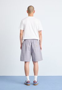 Back view of a person wearing a white t-shirt, light blue striped shorts, and blue sneakers with brown soles and white socks.