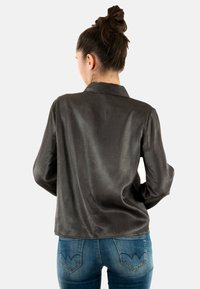 Camicia nera di raso con bottoni, colletto, maniche lunghe e orlo leggermente curvo. Indossata sopra jeans di denim blu con un design distintivo della tasca posteriore.