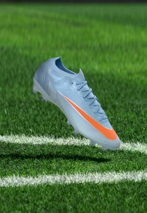 Crampon de football bleu clair avec un swoosh orange flottant au-dessus de l’herbe verte près d’une ligne blanche du terrain.
