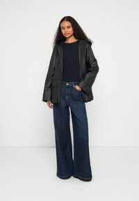 Fekete vízálló dzseki kapucnival, bőszárú kék farmerral párosítva. Laza illeszkedést és sima textúrát kínál.