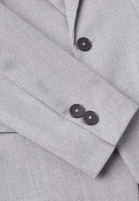 Jasnoszara tkanina o teksturowanym splocie, z mankietem z dwiema czarnymi guzikami i widocznymi akcentami przeszyć.