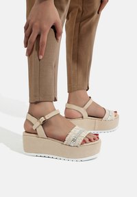 Sandali platform beige con tomaia in tessuto testurizzato, cinturino alla caviglia regolabile e design impreziosito da piccoli dettagli decorativi in perline.