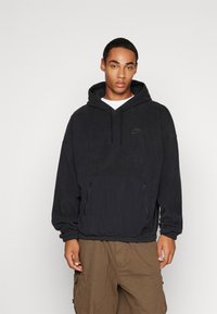 Črna kapuca s kengurujskim žepom, elastičnim robom in subtilnim logotipom. Narejena iz mehkega materiala z sproščenim krojem. Kapuca ima vrvice.