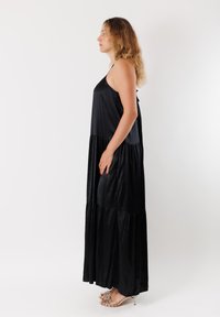 Abito maxi nero senza maniche con design a strati. Realizzato in tessuto morbido, presenta una silhouette fluida e un dettaglio con legatura sul retro.