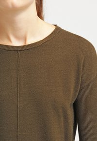 Suéter de punto verde oliva con un escote redondeado, textura suave y detalles acanalados en las mangas y el dobladillo.