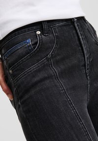 Crne traperice od denima imaju slim-fit dizajn s kontrastnim šavovima. Prednji džep ima plavu akcentnu šavnicu. Klasičan stil s pet džepova.