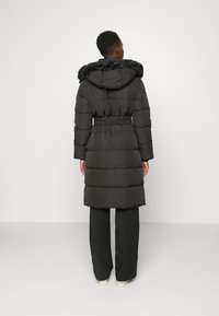 Černá péřová bunda s kapucí z umělé kožešiny, páskem v pase a vertikálním prošíváním. Sahl spíše k polovině lýtek a je kombinována s černými kalhotami s širokými nohavicemi.