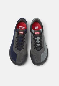 Twee paar sneakers, één marineblauw en één grijs, van bovenaf weergegeven. Elk heeft een zwart veterontwerp en rode binnensolen met merklabels.