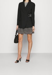 Svart skräddarsydd blazer med bältdetalj, kombinerad med ett mönstrat svartvitt minikjol. Accessoarer med en liten svart väska och klackar.