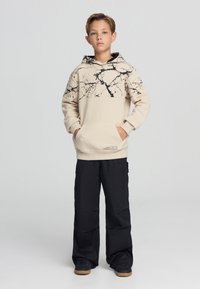 Hoodie beige con motivo in marmo nero sulla metà superiore, tasca a marsupio e orlo a costine; abbinato a pantaloni cargo neri e sneakers nere.
