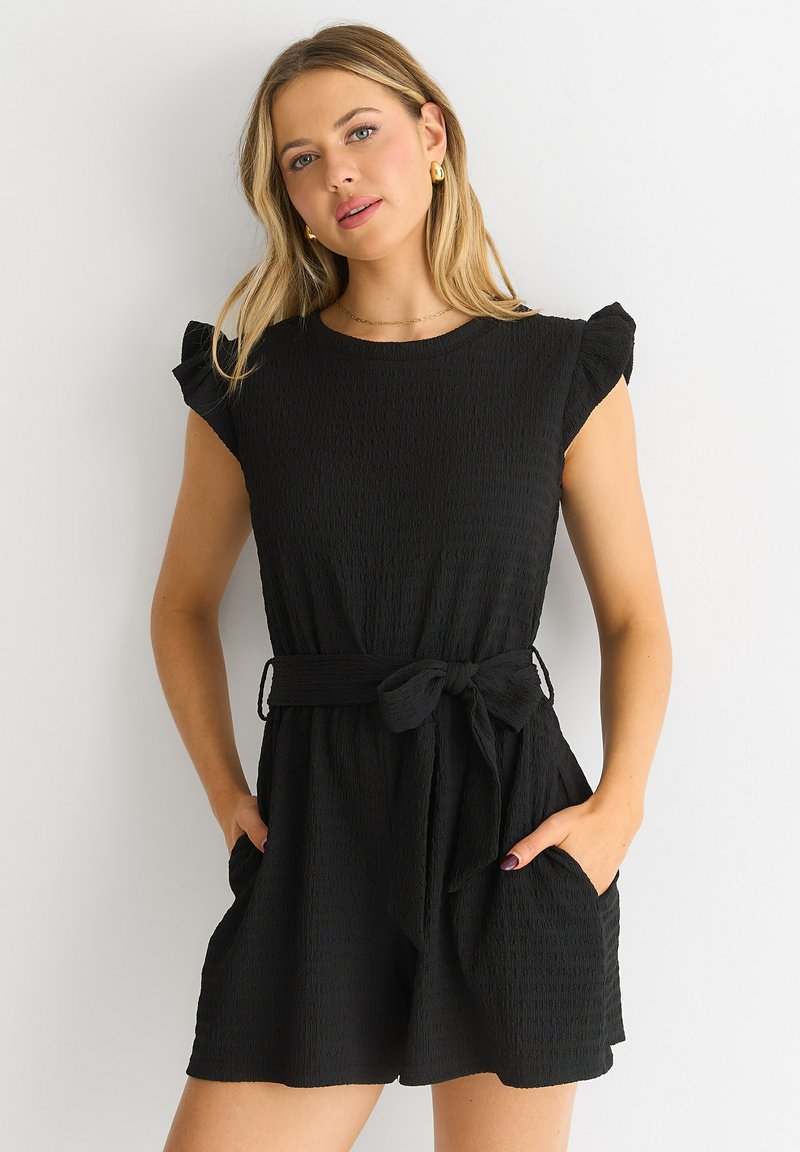 Zwarte mouwloze romper met gerimpelde schouderdetails, textuurstof, een aansluitende taille met een strikceintuur en zijzakken.