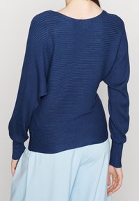 Granatowy sweter dzianinowy z szeroką szyją i luźnymi rękawami, uzupełniony gładką teksturą.