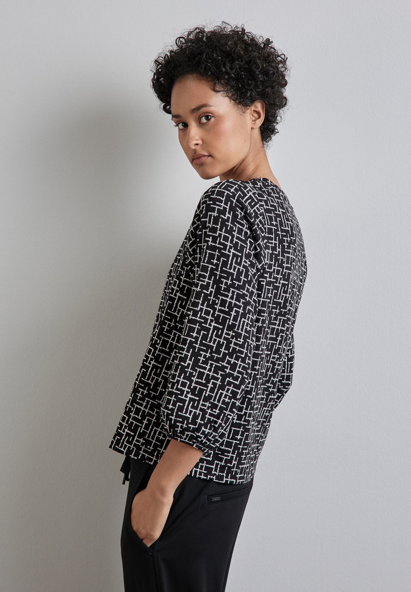 Schwarz-weißer gemusterter Oberteil mit Dreiviertelärmeln, strukturiertem Stoff, rechteckigen Designelementen und einer lockeren Passform.
