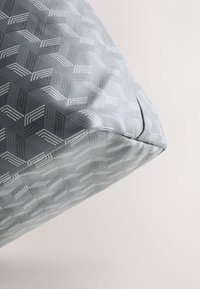 Tissu bleu-gris avec des motifs géométriques blancs en cubes couvrant un coussin d'angle ou un meuble rembourré.