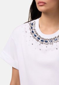 Witte T-shirt met een ronde halslijn, voorzien van een decoratieve kraag met bloemen van blauwe en heldere kristal accenten, zachte stof textuur.