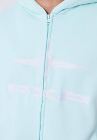 Felpa con zip color verde menta, con logo ricamato bianco. Tessuto morbido, cappuccio con cordino e zip frontale creano un design casual.