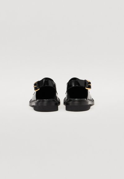 Black patent leather sandals with a rounded toe, adjustable ankle strap featuring a gold buckle, and a flat rubber sole.
