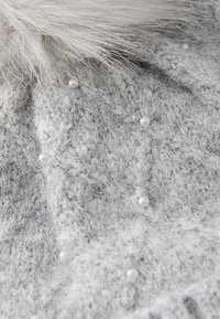 Tessuto a maglia grigio con una texture soffice, caratterizzato da piccole perle bianche incorporate e una rifinitura in pelliccia nella parte superiore.