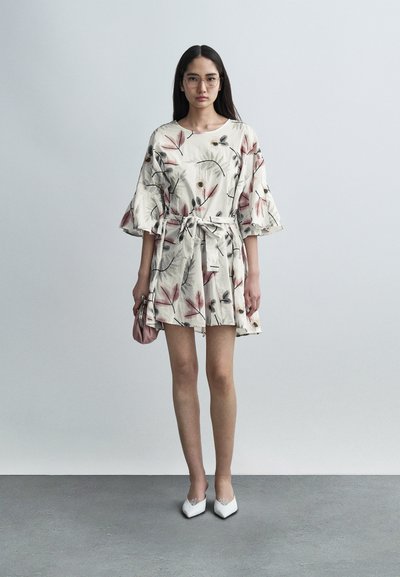 Φόρεμα με λουλουδάτο σχέδιο σε κρεμ απόχρωση, με φαρδιά μανίκια και ζώνη στη μέση. Συνδυασμένο με λευκά μυτερά παπούτσια και μικρή ροζ τσάντα. Λεία υφή.