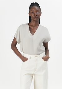 Lichtgrijze, kortärmelige blouse met een V-hals ontwerp. Draagt met crèmekleurige high-waisted jeans, met een gladde textuur en minimale accenten.
