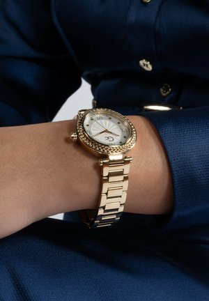 Orologio color oro con una ghiera testurizzata a corda, quadrante bianco e numeri romani. Presenta un robusto bracciale in metallo dorato con maglie rettangolari.