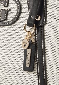 Sac à main noir et blanc à motifs avec des accents en simili cuir. Équipé d'un porte-clés doré et d'une étiquette avec le logo "GUESS".