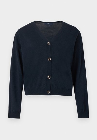 Καρντιγκάν σε σκούρο μπλε ναυτικό χρώμα με V-λαιμόκοψη, μακριά μανίκια και πέντε μεταλλικά κουμπιά στην μπροστινή πλευρά. Κατασκευασμένο από μαλακό πλεκτό υλικό, με κοντό σχέδιο.