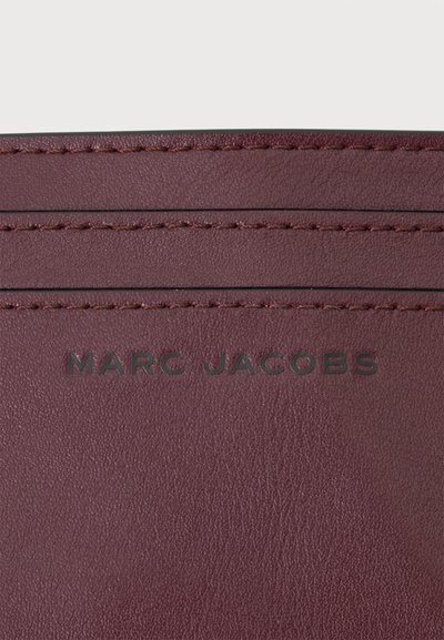 Тъмночервена кожена повърхност с три хоризонтално зашити линии и "MARC JACOBS" отпечатано в центъра.