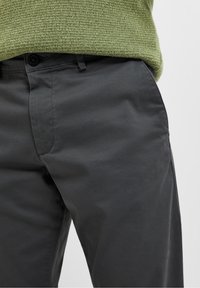 Donkergrijze broeken van gladde stof, met een klassiek model en een enkele voorkwast. Inclusief knoopsluiting en riemlussen.