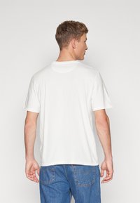 Tricou alb din bumbac, cu mâneci scurte, decolteu rotund și o croială lejeră. Vederea din spate evidențiază textura fină și designul simplu.