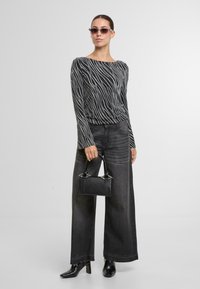 Černobíle pruhovaný top s dlouhým rukávem, černé široké kalhoty s vysokým pasem, černé boty na podpatku a malá černá kabelka s dekorativními uchy.