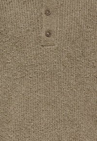Gros plan d’un tissu tricoté beige texturé avec deux boutons marron sur une fine patte de boutonnage au centre.