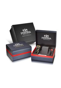 Črno-modra škatla za uro z rdečimi detajli. Znotraj je kamuflažna ura, siva blazina in pisalo. Ima logotip blagovne znamke in napis "Posebna izdaja".