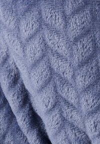 Una morbida coperta testurizzata di colore azzurro chiaro con un motivo a rombi in rilievo. Il tessuto appare soffice e accogliente, offrendo calore e comfort.