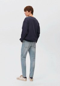 Sudadera azul marino de cuello redondo, jeans azul claro y zapatillas beige. Los jeans tienen un lavado sutil y bolsillos traseros. Corte casual.