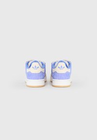 Par de sapatilhas Adidas em azul e bege, vistas de trás, com solas brancas e o logótipo trevo da Adidas nas abas do calcanhar.