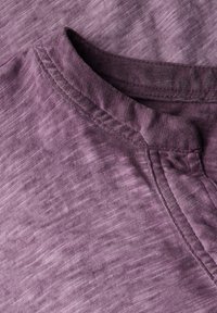 Kortærmet lilla T-shirt i blødt, struktureret stof. Har rund halsudskæring og diskrete, ujævne farvevariationer over det hele.