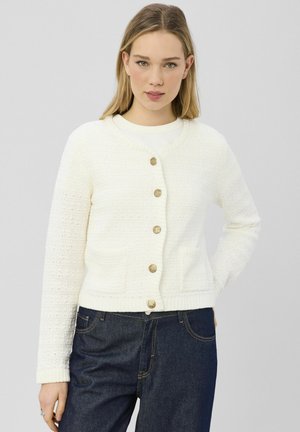 Cardigan blanc texturé avec un col rond, une fermeture à boutons sur le devant et des poches. Présente des poignets et un ourlet côtelés, ornés de boutons dorés.