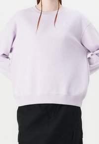 Lichtpaarse sweater van zacht materiaal, met een ronde hals, geribbelde boorden en zoom, en een wit logo op de borst.