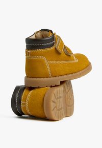 Stivali alla caviglia in suede giallo con colletto in pelle nera, cuciture bianche e cinturino in velcro. Suola in gomma resistente con battistrada testurizzato.