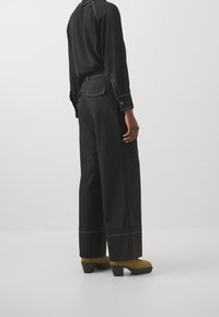 Černé kalhoty širokého střihu s bílým šitím, doplněné žlutými platformovými botami. Oblečení má na kalhotech zadní kapsu.