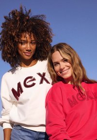 Dos sudaderas: una blanca con "MEX" burdeos y otra roja con "MEX" negra, ambas con un ajuste relajado y una textura de tela suave.