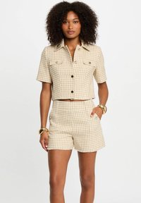 Chemise cropped à carreaux beiges avec des manches courtes et des boutons, assortie à un short taille haute avec poches latérales.