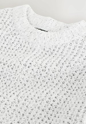 Hvid strikket sweater med en tekstureret overflade, med rund halsudskæring og sorte pletter gennem stoffet for ekstra detaljer.