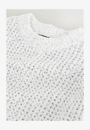 Balta megzta svajonė su tekstūruota paviršiumi, turinti apykaklę ir juodų dėmių visame audinyje papildomam akcentui.