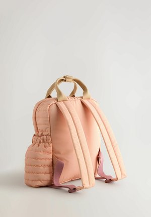 Pink padded backpack with beige handle, adjustable straps, side pocket, and soft texture. Features a compact, rounded shape with subtle stitching.